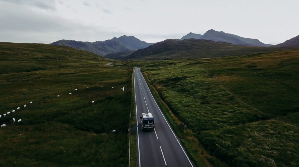 A campervan driving down a road in the mountains in Wales