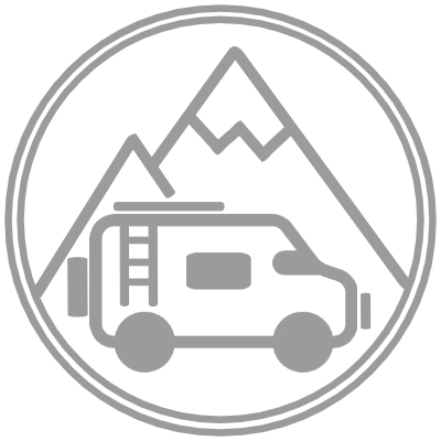 A circular logo features a line drawing of a camper van positioned in the foreground. Behind the van, there are two triangular mountain peaks, creating a backdrop. The entire design is enclosed by a thin circular border. The image is in grayscale.