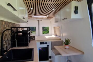 inside of the van, white interior with wood, black kitchen appliances, air vent